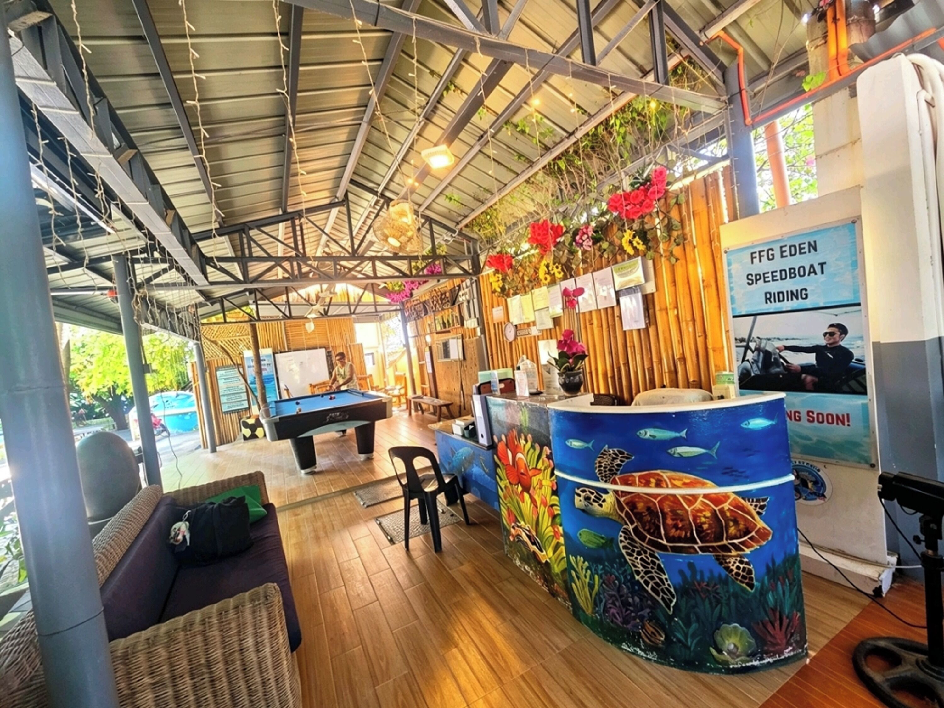 Una mesa de billar en una sala con pared de bambú, un cartel de lancha rápida y un mural de tortuga.
