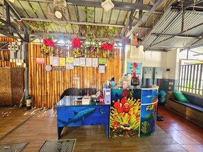 Zona de recepció amb fons de bambú, taulell de recepció amb mural submarí i zona de seients amb coixí verd.