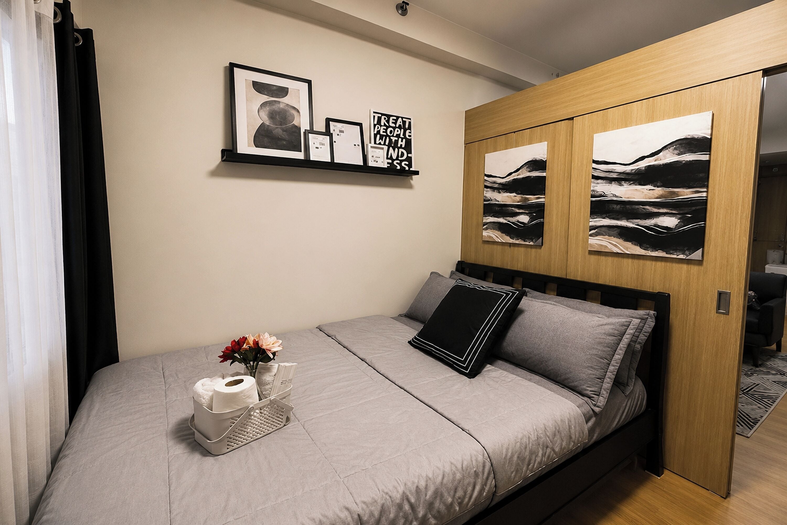 Une chambre à coucher avec un lit, une table de chevet ornée d’un vase et d’une boîte de mouchoirs, et deux tableaux encadrés accrochés au mur.