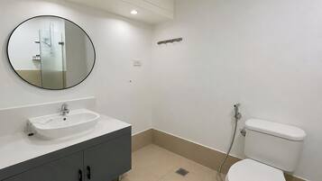 Une salle de bain avec un miroir rond, un lavabo, des toilettes et une douche.
