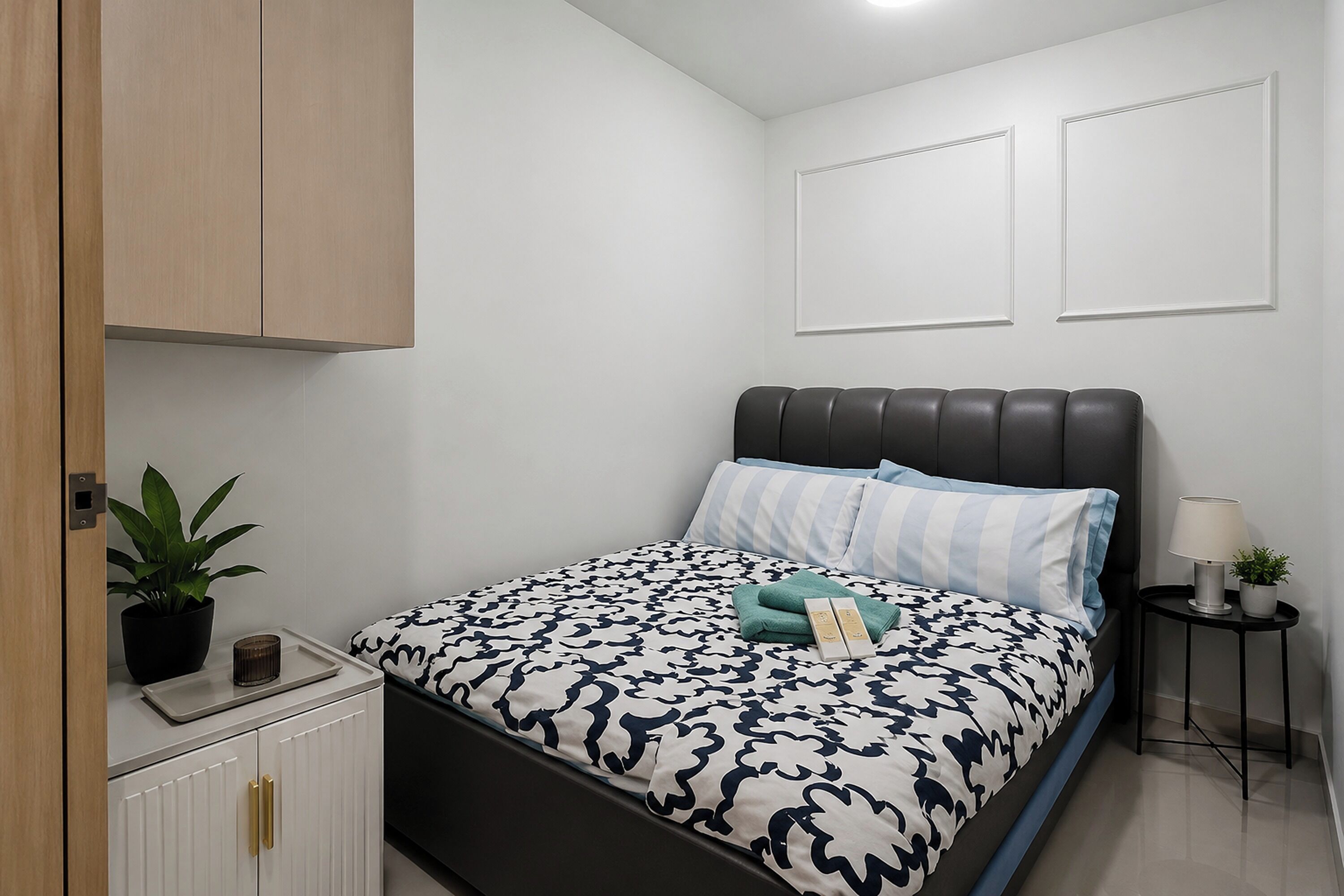 Un dormitorio con cama, mesita de noche, lámpara y planta en maceta.