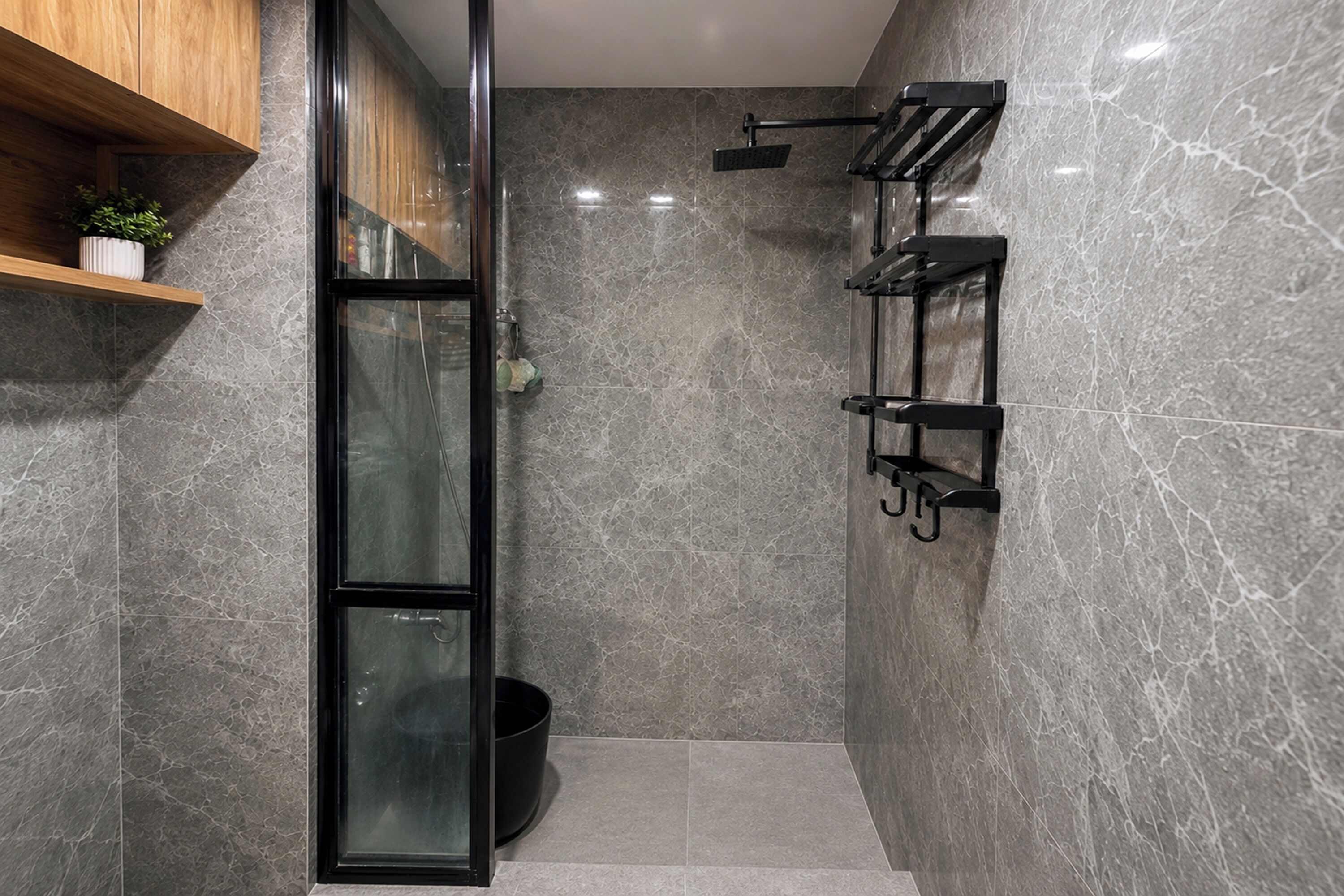 Un baño moderno con cabina de ducha de vidrio, un perchero negro y una estantería de madera con una planta.