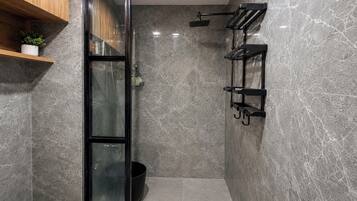 Un baño moderno con cabina de ducha de vidrio, un perchero negro y una estantería de madera con una planta.