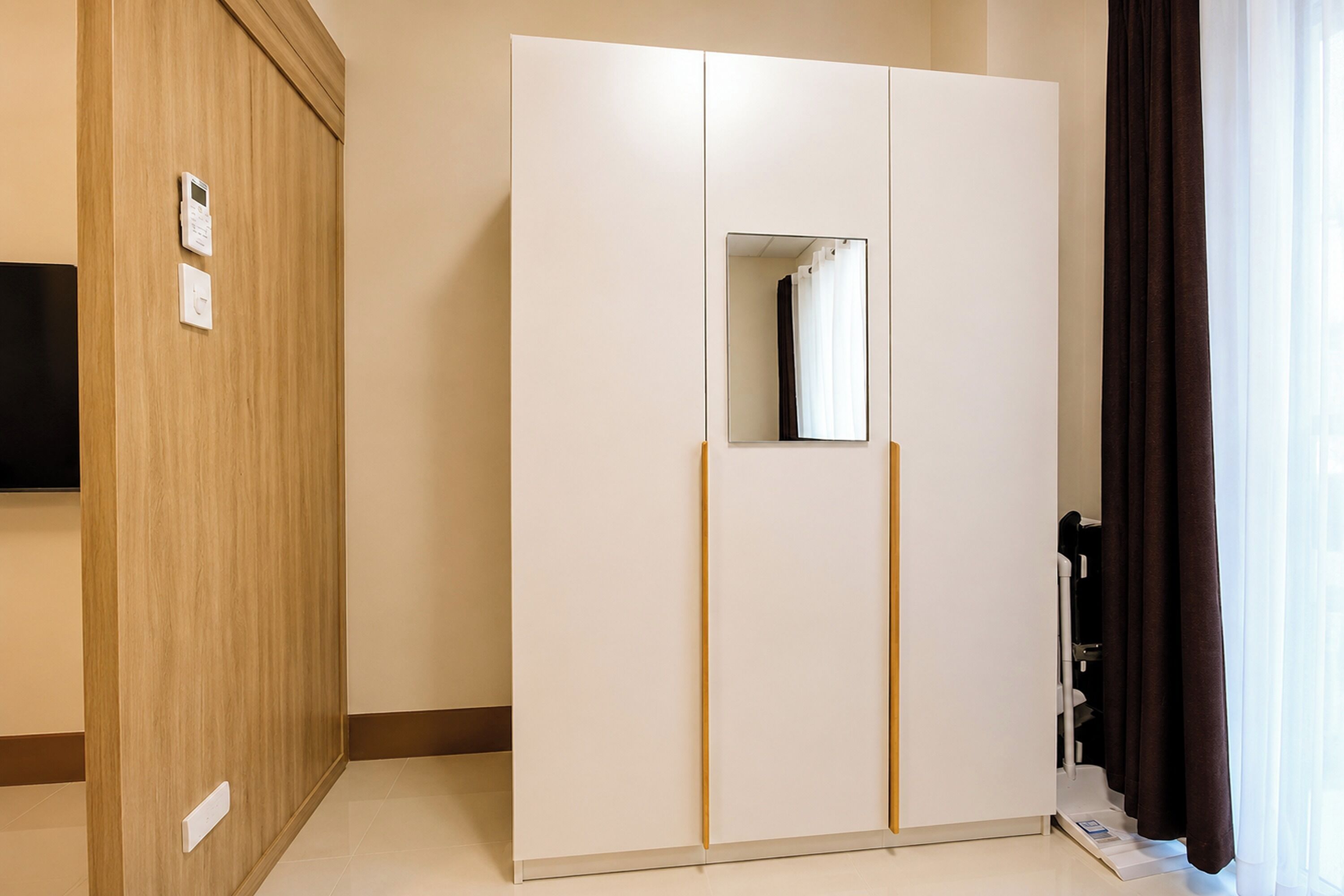 Una habitación con armario, espejo y ventana con cortinas.
