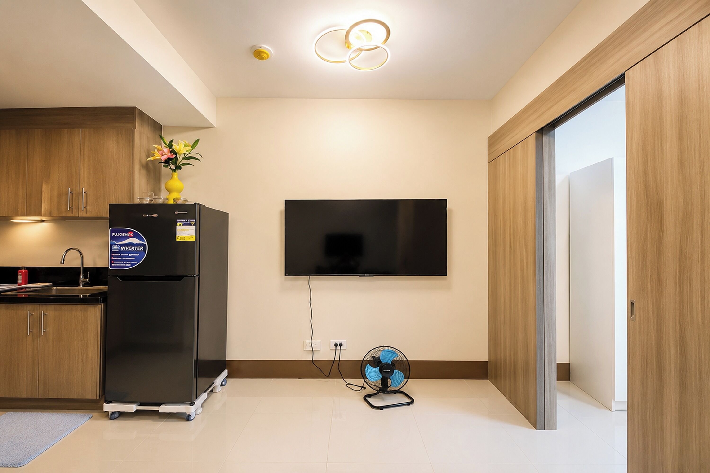 A modern kitchen with a built-in refrigerator, a wall-mounted TV, and a small fan on the floor.