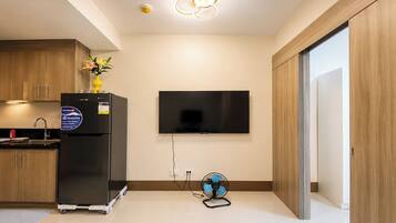 A modern kitchen with a built-in refrigerator, a wall-mounted TV, and a small fan on the floor.