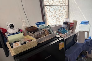A hotel room counter with a coffee maker, a toaster, a basket of snacks, a hairdryer, a bottle of hand soap, and a water jug. - Sleep Break Hostel Sathon (Bangkok)