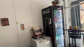 A vending machine with Coca-Cola branding, a small refrigerator, and a wooden shelf with various items. - Sleep Break Hostel Sathon (Bangkok)