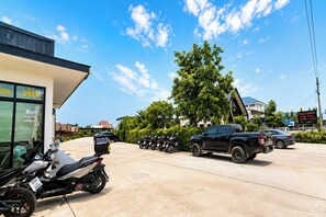 A parking area with motorcycles and a pickup truck, a building with a sign, and a tree.
