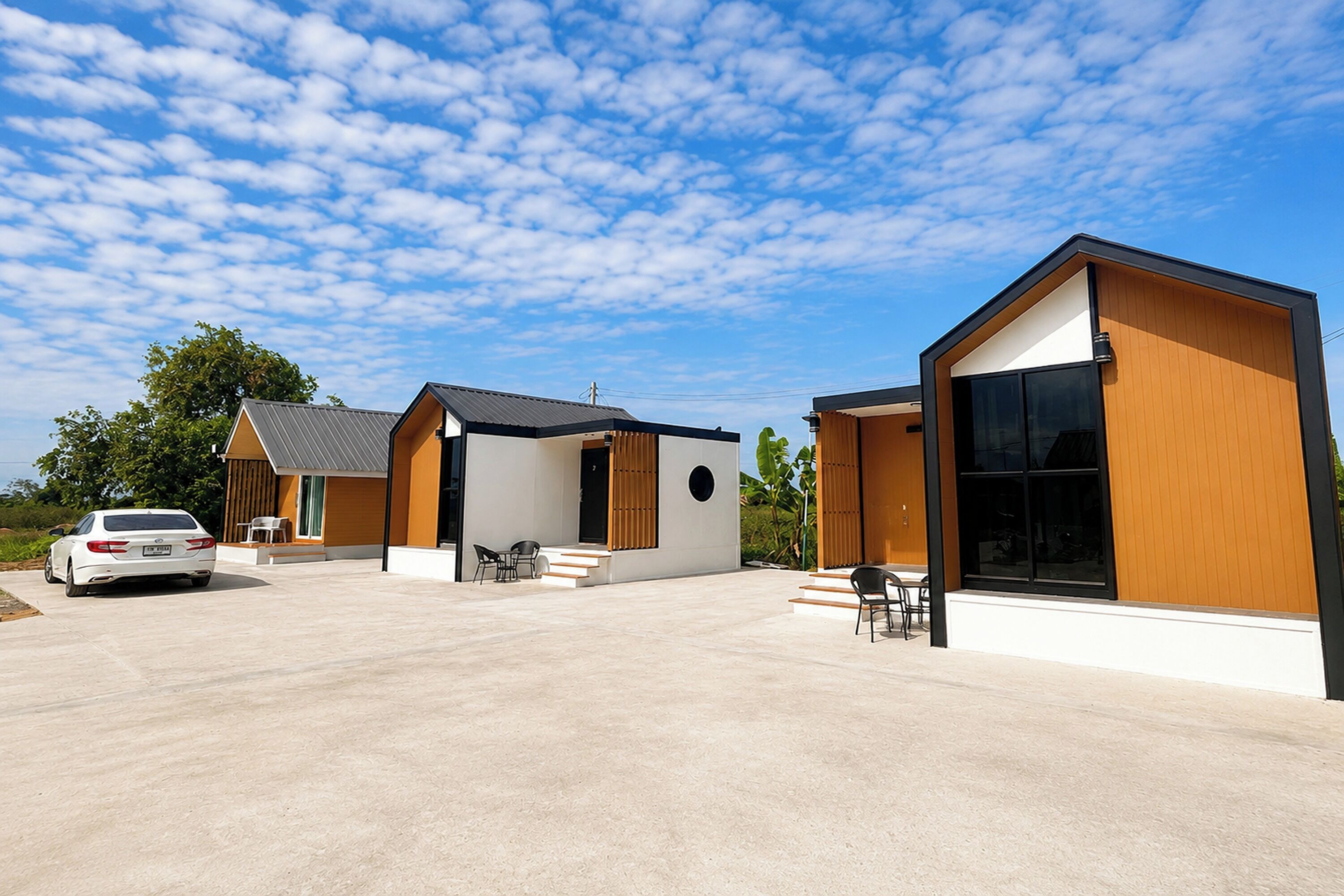 A modern building with a spacious outdoor area, a car parked in front, and a clear blue sky with clouds.