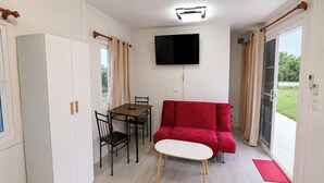 Ein kompakter Wohnraum mit einer Couch, einem Esstisch mit Stühlen, einem flachbildfernseher an der Wand und einer Glastür zum Außenbereich.
