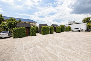 A parking area with a row of neatly trimmed hedges, a white building with a blue roof, and a silver car parked in the lot.