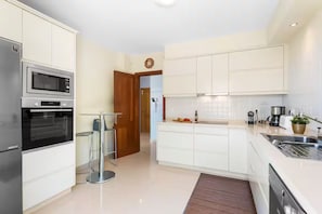 Eine moderne Küche mit weißen Schränken, einem Backofen, einer Mikrowelle, einer Kaffeemaschine und einem Spülbecken.