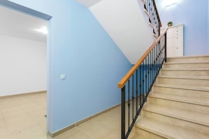 Eine Treppe mit Holzhandlauf und schwarzen Spindeln, die zu einer Zwischenebene mit einem weißen Schrank und einem Blumentopf führt.