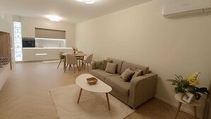 A modern living room with a sofa, coffee table, and dining area. - Helena Living Harmony (Varna)