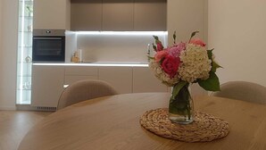 A modern kitchen with a built-in oven and a dining area with a round table and chairs. - Helena Living Harmony (Varna)