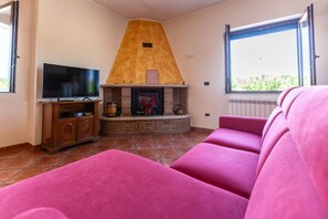 A living room with a fireplace, a television, and a large pink sofa. - Hospitality as a Value: ​There are places that keep alive the spirit of those who loved them. (Giardoni)