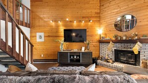 Ein gemütliches Wohnzimmer mit Kamin, einem an der Wand montierten Fernseher und einer Treppe, die zu einer oberen Ebene führt.
