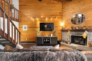 A cozy living room with a fireplace, a television mounted on the wall, and a staircase leading to an upper level. - Wood Fireplace | Hot Tub | Pool in Summer | Arcade Games (Steamboat Springs)