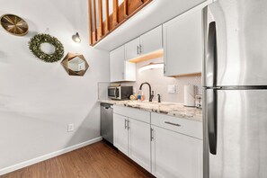 A modern kitchen with white cabinets, a stainless steel refrigerator, a microwave, and a sink with a black faucet. - Wood Fireplace | Hot Tub | Bust Stop at Condo | Arcade Games (Steamboat Springs)