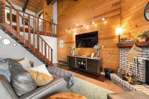 A wooden interior with a staircase, a flat-screen TV, a fireplace, and a sofa. - Wood Fireplace | Hot Tub | Bust Stop at Condo | Arcade Games (Steamboat Springs)