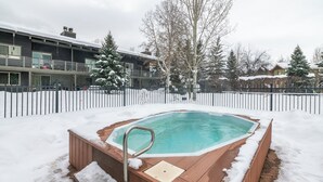 Ein Whirlpool, umgeben von Schnee, mit einem Holzboden und Metallgeländern.