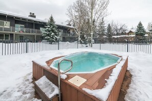 A hot tub surrounded by snow, with a wooden deck and metal railings. - Wood Fireplace | Hot Tub | Pool in Summer | Arcade Games (Steamboat Springs)