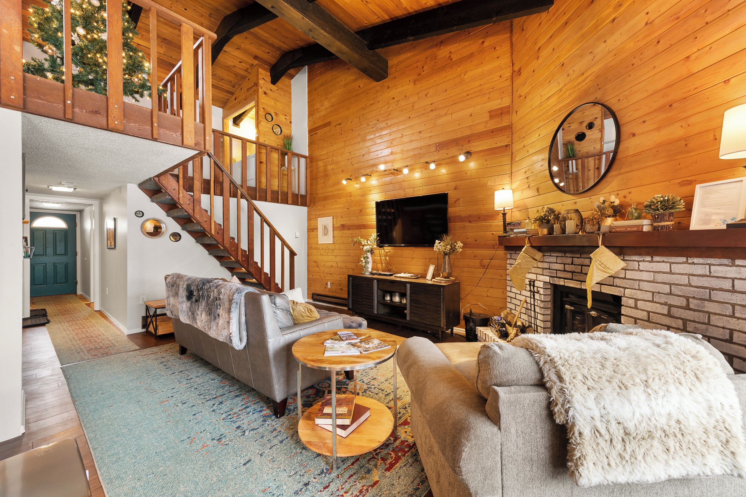 A cozy living room with a fireplace, a staircase, and a television mounted on the wall.