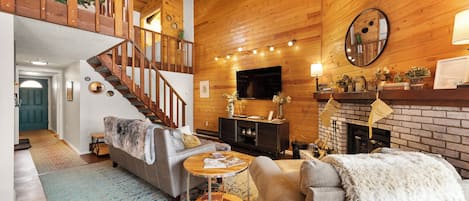 A cozy living room with a fireplace, a staircase, and a television mounted on the wall.