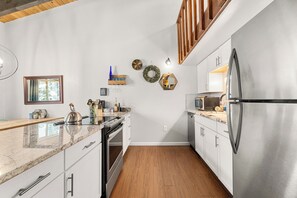 A modern kitchen with white cabinetry, a stainless steel refrigerator, and a wooden floor. - Wood Fireplace | Hot Tub | Bust Stop at Condo | Arcade Games (Steamboat Springs)
