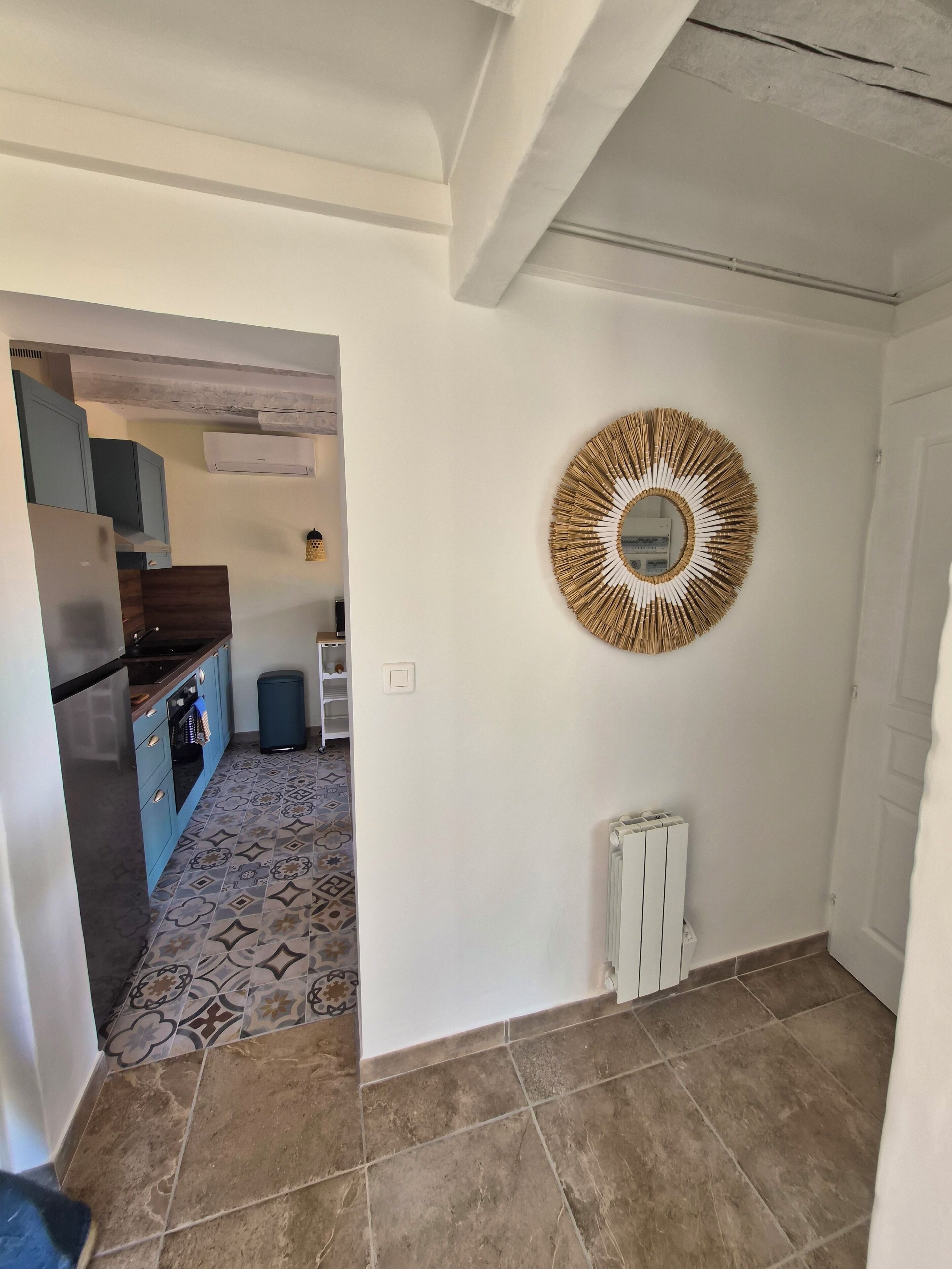 Cocina con armarios azules, piso estampado y un espejo decorativo en la pared.