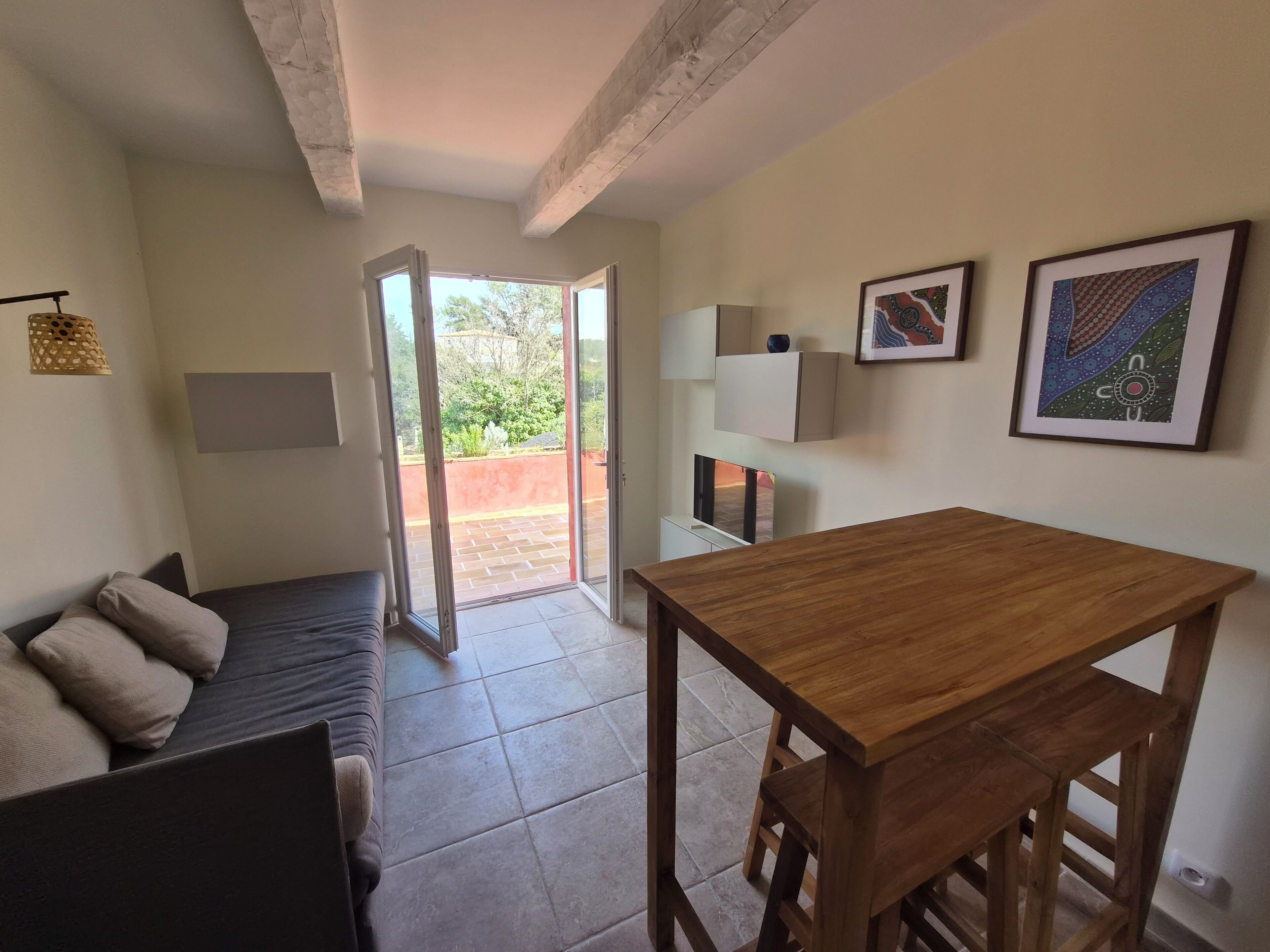 Une pièce avec une table en bois, un canapé et une porte-fenêtre coulissante donnant sur un espace extérieur.