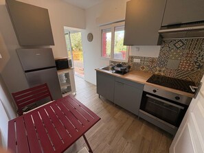 Eine kompakte Küche mit Kühlschrank, Mikrowelle, Backofen und einem Fenster mit Blick ins Freie.