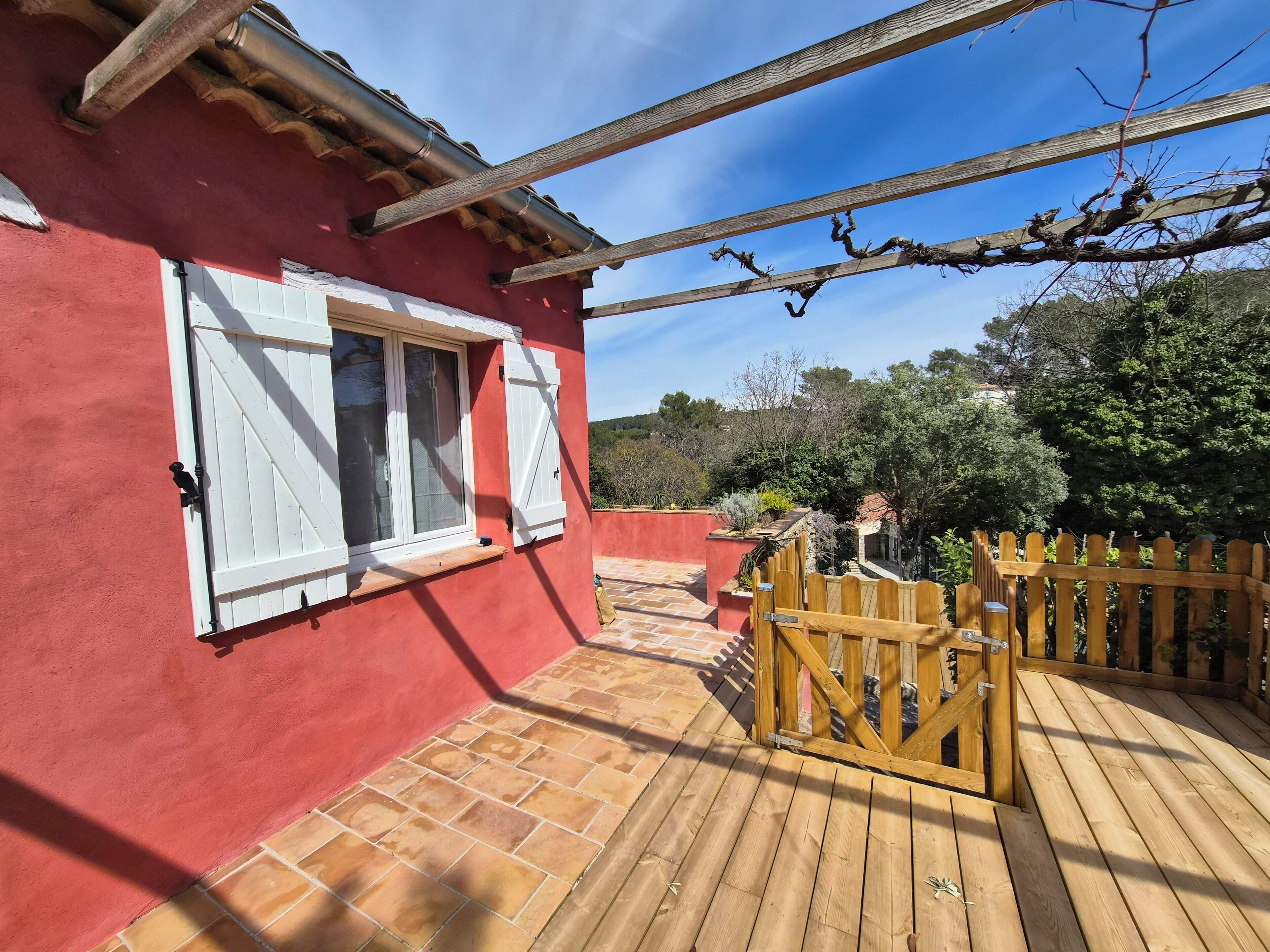 Un bâtiment rouge avec des volets blancs, une terrasse en bois et une clôture en bois.