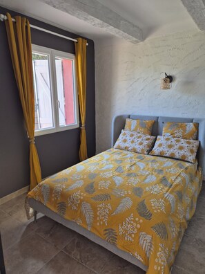 Ein Schlafzimmer mit Bett, Vorhängen, einem Fenster und einer Wandleuchte.