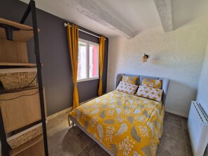 Une chambre à coucher avec un lit, une fenêtre avec des rideaux, un luminaire fixé au mur et un radiateur.
