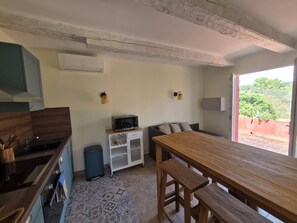 Eine kompakte Küche mit Mikrowelle, Spüle und Schränken. Es gibt einen kleinen, weißen Schrank mit Weinflaschen und einem Mülleimer. Im Vordergrund steht ein Holztisch mit Bänken.