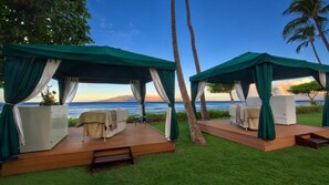 Duas cabanas ao ar livre com vista para o oceano, cada uma com uma cama e uma pequena mesa.