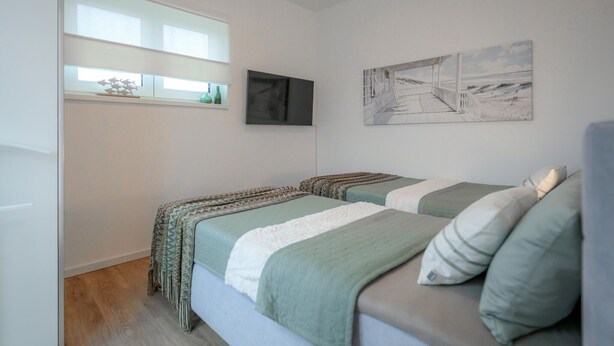 Et soveværelse med to senge, et vindue, et maleri og et fladskærms-tv.
