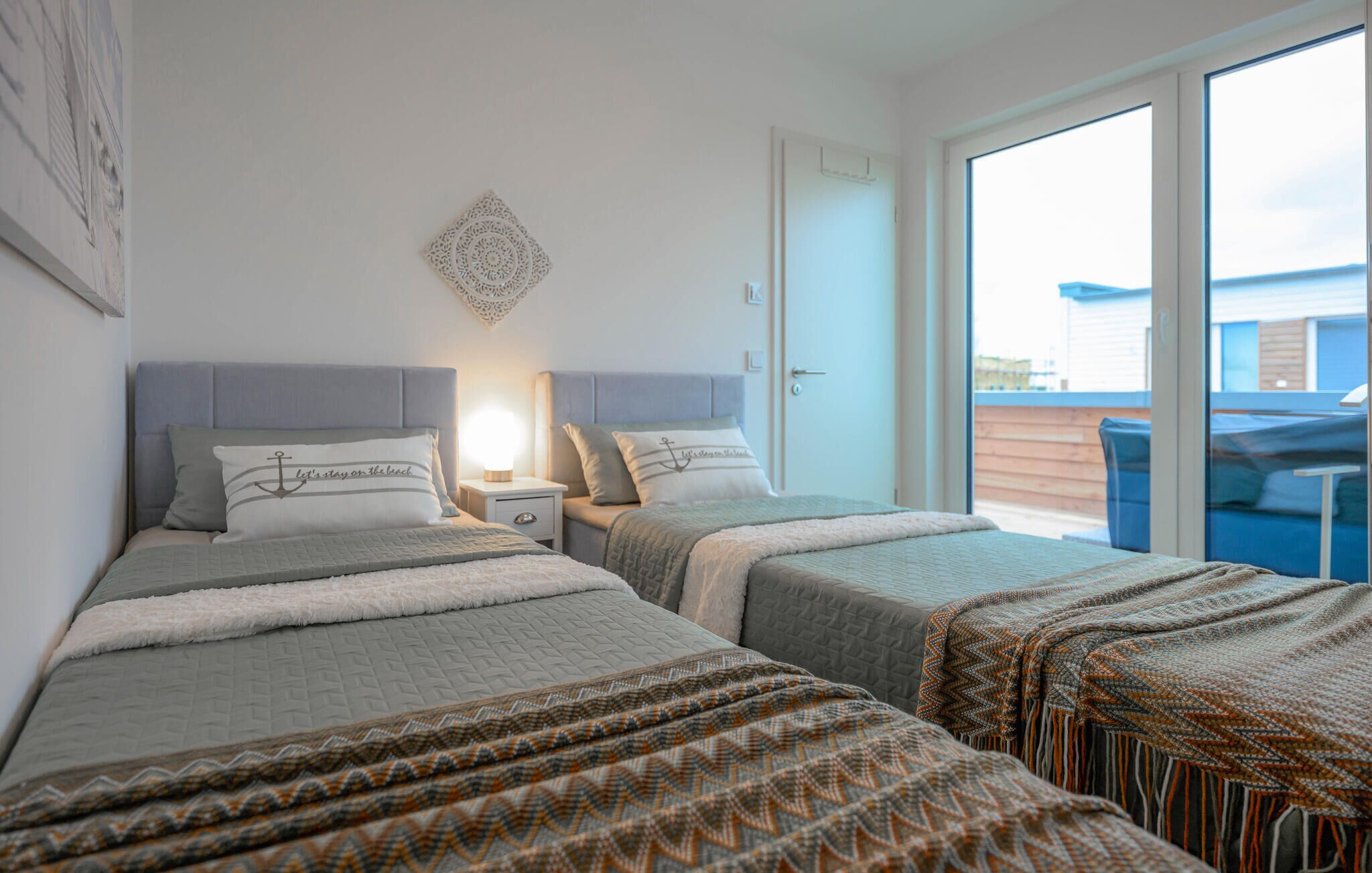 Ein Hotelzimmer mit zwei Betten, einem Nachttisch, einem an der Wand befestigten dekorativen Gegenstand und einer Glastür, die zu einem Außenbereich führt.