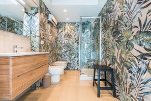 A modern bathroom with a wooden vanity, two toilets, a glass shower enclosure, and a tropical leaf-patterned wall. - Residenza Partanna by Napoliapartments (Naples)