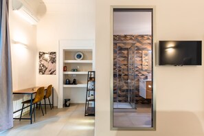 Ein modernes Zimmer mit Essbereich, Fernseher und einer Dusche mit geometrischen Wandfliesen.