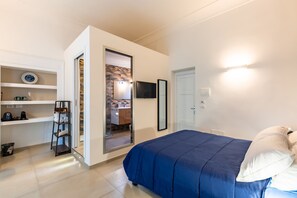A bedroom with a bed, a wardrobe, a shelf with towels, a TV, and a door leading to a bathroom. - Residenza Partanna by Napoliapartments (Naples)
