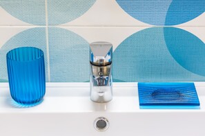 A bathroom sink with a blue glass vase, a metallic faucet, and a blue glass tray. - Mergellina in Napoli (Naples)