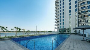 Una piscina con solárium de baldosas, rodeada por un edificio de gran altura con balcones.