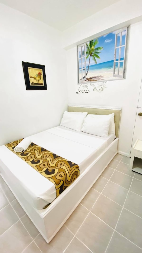 Un dormitorio con cama, ventana con vista a la playa, un cuadro enmarcado en la pared y una puerta.