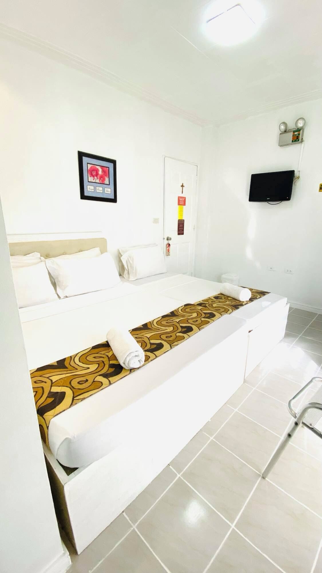 A hotel room with a bed, a television, a framed picture, and a door with a sign.