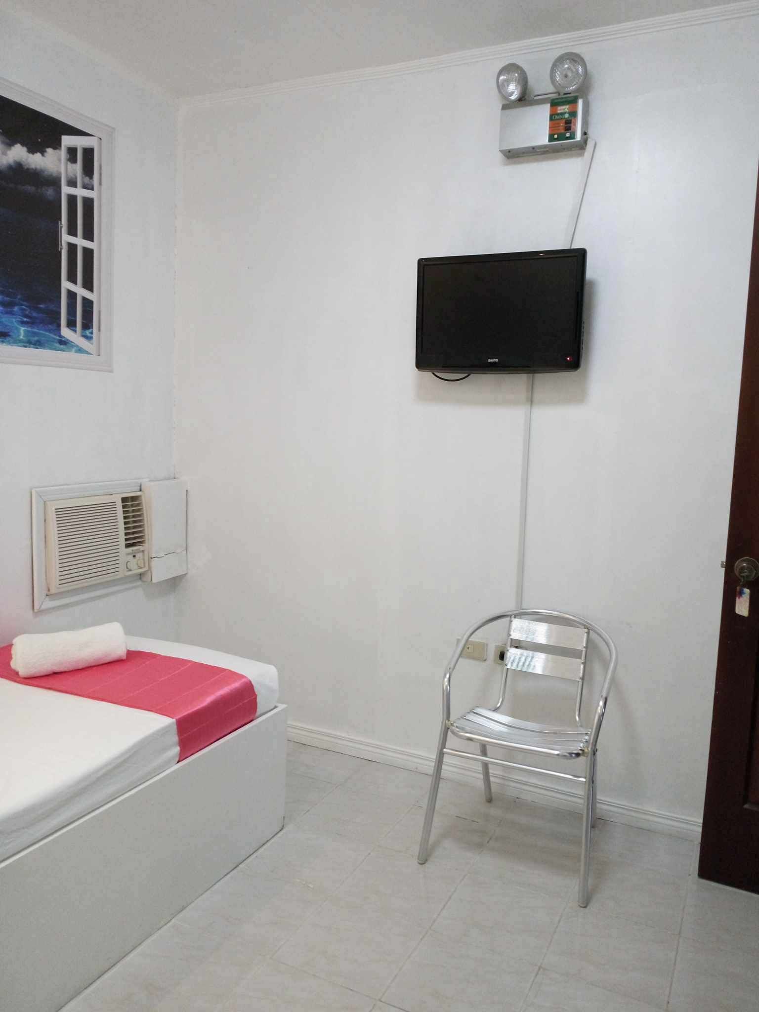 Une pièce comprenant un lit, une chaise, un téléviseur fixé au mur et une fenêtre donnant sur le ciel.
