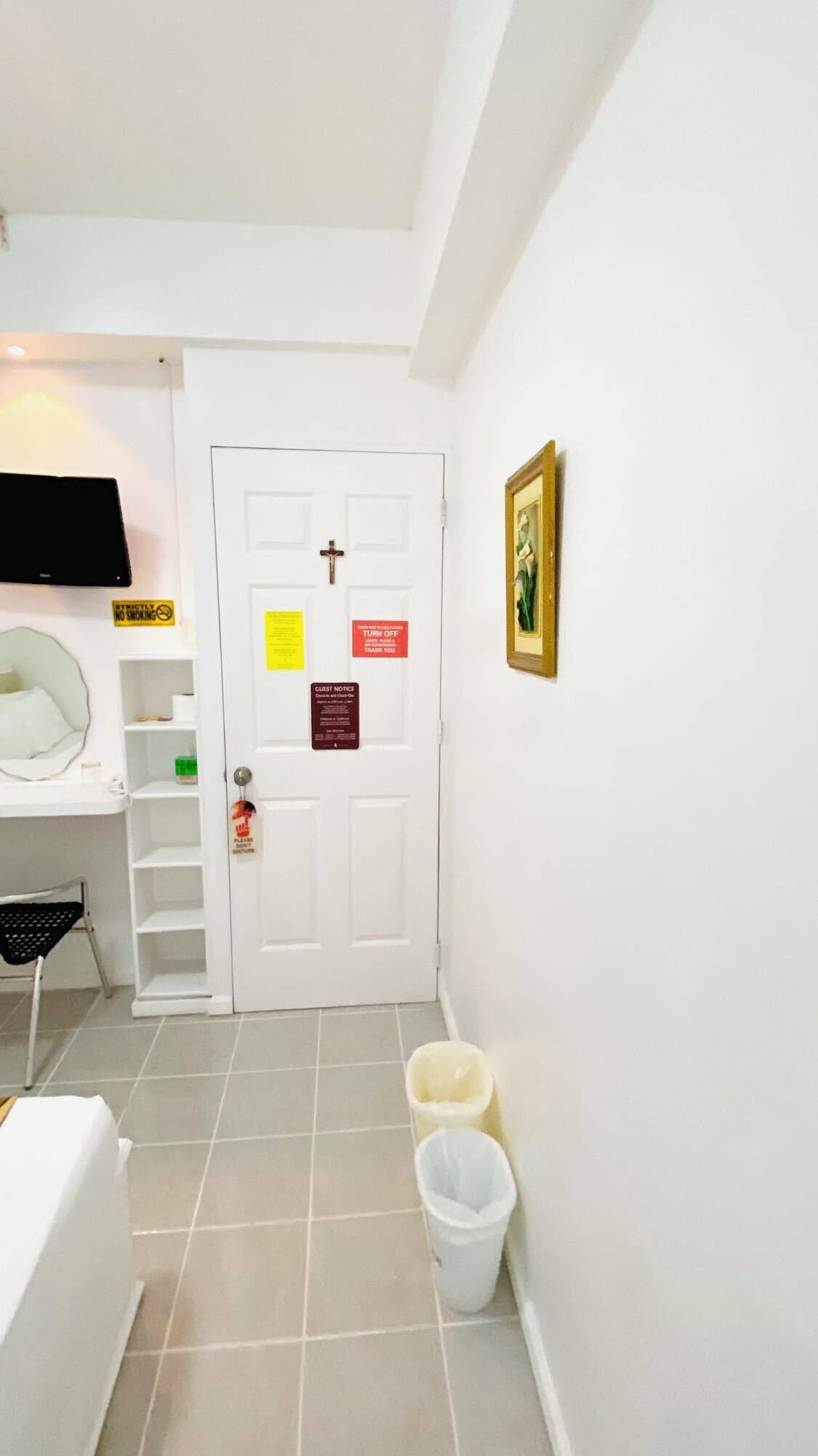 Habitación de hotel con una puerta blanca, un televisor en la pared, una cama, un escritorio y un cesto de basura.