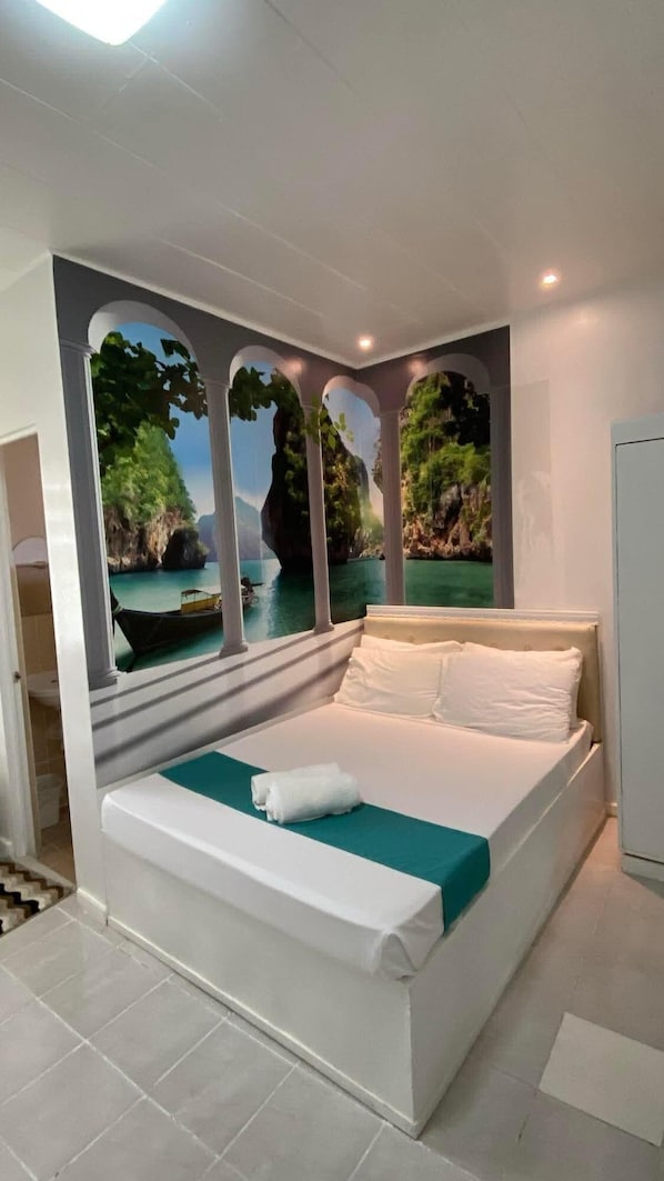 A bedroom with a bed, a view of a tropical landscape through a window, and a white ceiling.